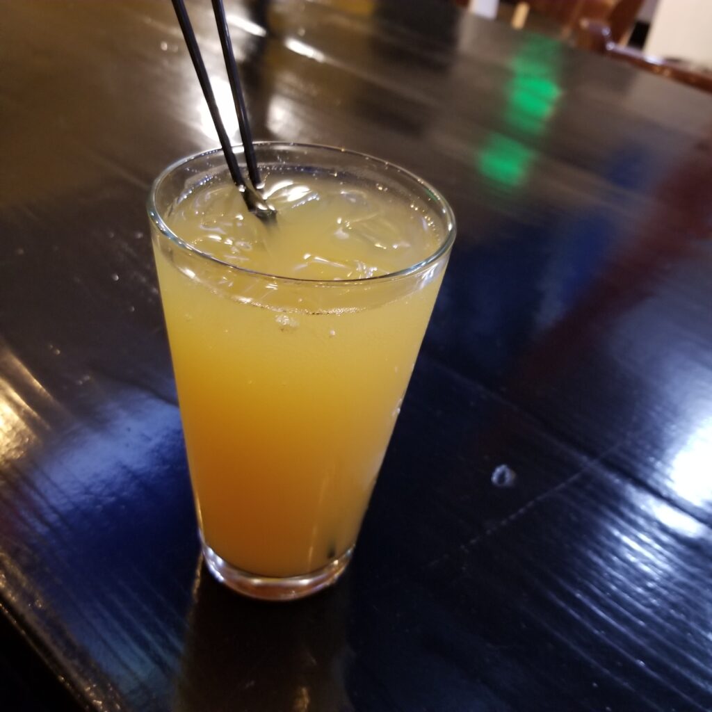 a pint glass filled with ice and an orange liquid sits on a glossy black bar